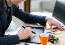 The Best Spaces for Launching Your Comic Book Business A person sitting at a desk with a paint set and mug. They hold a digital pen in their right hand while using a tablet.