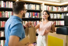 Using Printed Graphics To Drive Visitor Engagement A cashier hands a brown paper bag with purchased books to a customer wearing glasses at the checkout desk.