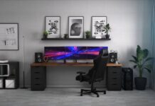 Features That You Need To Have in Your Gaming Room A black gaming chair sits in front of a large desk with three computer monitors inside a home office.