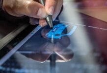 6 Essential Steps To Make Digital Comic Art A hand using a silver stylus to draw a blue car on a tablet screen, while its reflection appears on the glass surface.