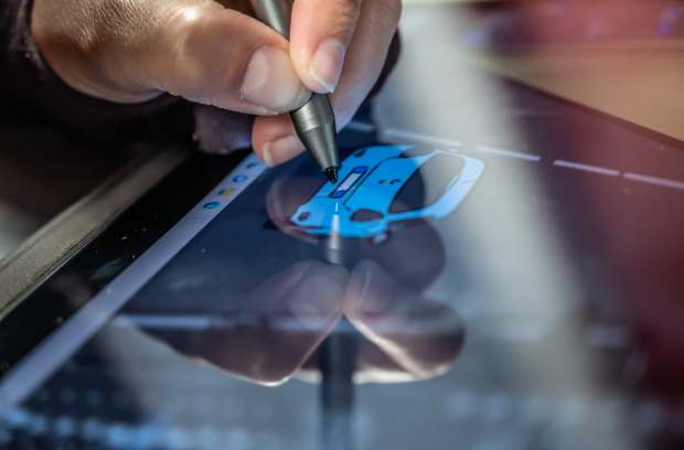 wiseteksolutions-inc-380623-drawing-on-tablet-image1(1) A hand using a silver stylus to draw a blue car on a tablet screen, while its reflection appears on the glass surface.