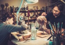 Create the Perfect Workshop for Building Cosplay Props Two people sit across from each other at a table with paintbrushes and materials on it and paint props.