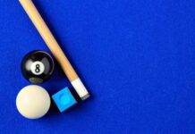 Various Materials Used in Pool Cue Creation A close-up shows a pool cue, a black eight pool ball, a white pool ball, and blue cue chalk sitting on blue felt.