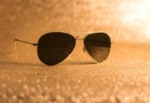 Most Famous Aviator Sunglasses in Movies A pair of aviator sunglasses resting against a golden background with dots of light reflecting off the lenses.