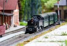 Considerations To Make for Your Model Railroad A close up of a small model train going down a railroad in front of a model train station with small people figures.