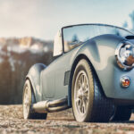 4 Muscle Cars Made Famous by Hollywood Movies A gray convertible classic car with chrome details and round headlights parked in front of snowy mountains.