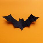 Tips for Making a Cosplay Batman Utility Belt A black carving in the shape of a bat. The bat-shaped carving rests on a yellow background, with shadows behind the wings.