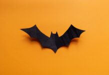 Tips for Making a Cosplay Batman Utility Belt A black carving in the shape of a bat. The bat-shaped carving rests on a yellow background, with shadows behind the wings.