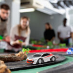 Why Slot Car Racing Is the Ultimate Hands-On Hobby A closeup of a white and red slot car on a track. There are several excited onlookers watching the race in the background.