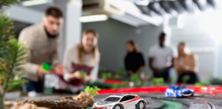 Why Slot Car Racing Is the Ultimate Hands-On Hobby A closeup of a white and red slot car on a track. There are several excited onlookers watching the race in the background.