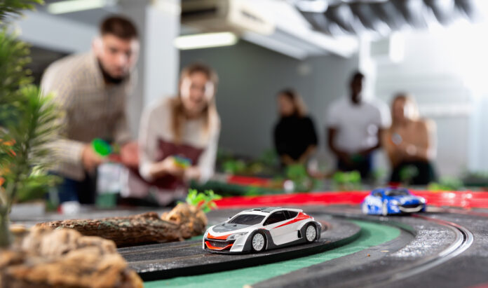 Slot car racing track. Emotional players drive toy cars A closeup of a white and red slot car on a track. There are several excited onlookers watching the race in the background.