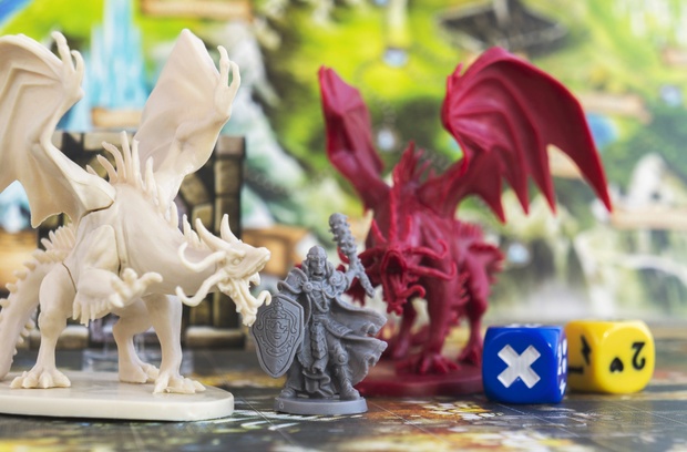 Three 3D printed miniatures of two dragons and a mage placed beside two dice on a map, all set against a detailed background. Three 3D printed miniatures of two dragons and a mage placed beside two dice on a map, all set against a detailed background.