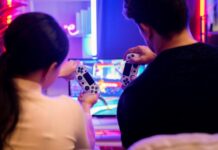 How To Build a Functional Gaming Space Anywhere A guy and girl sitting close to each other on the couch while holding gaming controllers. They are playing a fighting game.