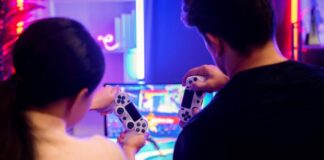 How To Build a Functional Gaming Space Anywhere A guy and girl sitting close to each other on the couch while holding gaming controllers. They are playing a fighting game.