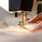 Understanding Thread Tension for Flawless Sewing Results A close-up view shows a person pushing white fabric through the sewing needle of a sewing machine.
