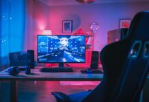 How To Build a Gaming Room on a Tight Budget A modern desk with a gaming chair in a colorfully lit room. The desk has a PC desktop, speakers, and gaming headphones.