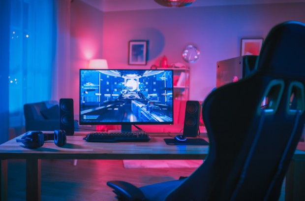 How To Build a Gaming Room on a Tight Budget A modern desk with a gaming chair in a colorfully lit room. The desk has a PC desktop, speakers, and gaming headphones.