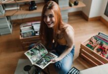 Essential Tips for Moving Your Comics and Collectibles A smiling woman with reddish hair sits on a wooden floor as she holds an open comic book. Crates of comics sit behind her.