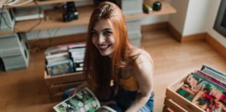 Essential Tips for Moving Your Comics and Collectibles A smiling woman with reddish hair sits on a wooden floor as she holds an open comic book. Crates of comics sit behind her.