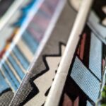 How to Protect Your Artwork And Comics at Home A closeup of a collection of comic books all stacked next to each other, with colorful, textured papers.